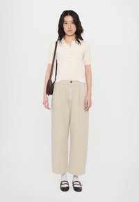 Light cream short-sleeve polo with buttons, paired with loose beige trousers. Completing the look are brown strap shoes and white socks.