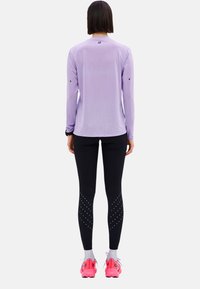Helles lila langärmliges Shirt mit Rundhalsausschnitt, schwarze Leggings mit gemusterten Akzenten und rosa Sportschuhe mit grauen Schnürsenkeln.