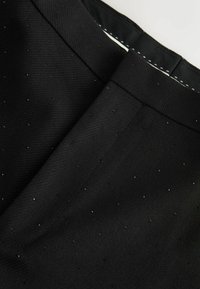 Pantaloni din țesătură neagră cu o textură netedă, cusături subtile și mici puncte reflective dispersate pentru detaliu și accent.
