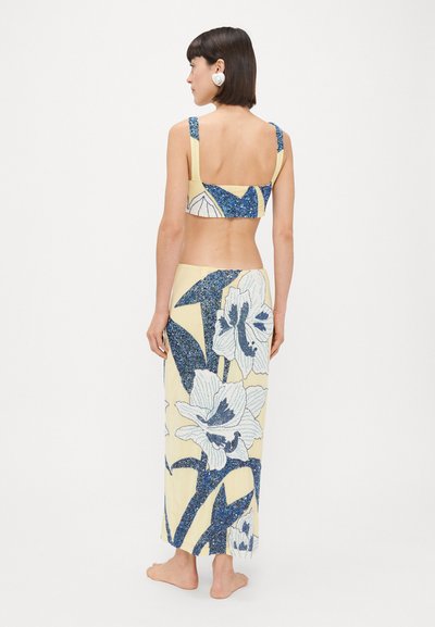 Conjunto de dos piezas que incluye un top corto amarillo y una falda a juego, decorados con patrones florales azules y acentos texturizados.