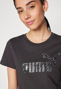 Camiseta de algodón negra con un logo de rayas de cebra en plata y negro texturizado y reflectante que dice "PUMA" junto a un gráfico de un puma saltando.