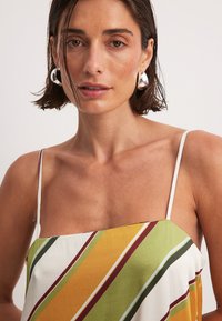 Robe nuisette en satin avec des rayures diagonales jaune, vert et bordeaux, des bretelles fines en spaghetti et une texture lisse et fluide.