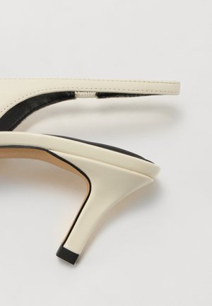 Cremefarbener High-Heel-Slingback-Schuh mit schwarzem Rand und spitzer Zehe, seitlich auf weißem Hintergrund dargestellt.