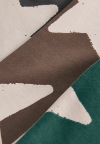 Textilstoff mit weicher Textur, der abstrakte Formen in Schwarz, Braun und Grün auf einem hellbeigen Hintergrund aufweist.