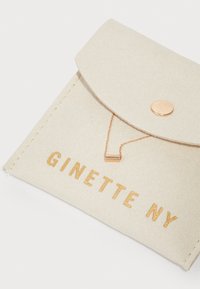 Borsa in feltro beige con chiusura a pattina, caratterizzata da testo in oro embossato "GINETTE NY" e un dettagli in catena rosé con un accento rettangolare.
