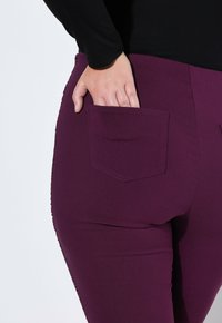 Fioletowe spodnie o gładkiej fakturze, z tylną kieszenią i wyszywanymi detalami po bokach. Pas znajduje się na naturalnej wysokości talii.