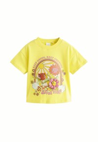 Gul bomulds T-shirt med korte ærmer, der har et farverigt trykt design af blomster, en smilende sol, og teksten "Bliv ved, Bliv ved med at vokse!"