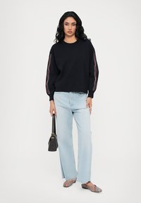 Navy sweater with patterned accents on sleeves, light blue straight-leg jeans, striped shoes, and a black handbag. Smooth texture throughout.