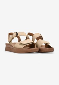 Sandalias beige con dos correas anchas y una hebilla. Textura suave de ante, diseño de punta abierta y una suela moldeada marrón para mayor comodidad.
