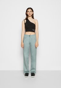 Top crop preto de um ombro, combinado com umas calças de cordão verdes claras e ténis pretos. As calças apresentam uma textura suave e um corte reto.