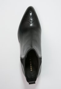 Musta nahkasaapas nilkkaan, jossa on terävä kärki, koristeelliset rei'itykset edessä, joustavat sivupaneelit ja vetolenkkki kantapäässä.