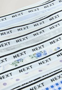 Rangées de ceintures en tissu avec le mot « NEXT » en texte noir, présentant différents motifs tels que des fleurs, des pois et des carreaux.