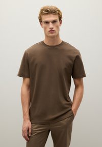 T-shirt marrone a maniche corte in cotone, con colletto girocollo e vestibilità rilassata. Texture liscia senza motivi o accenti visibili.
