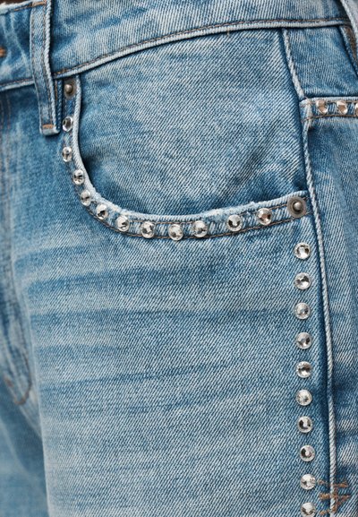 Τσέπη ελαφρώς μπλε τζιν με ασημένιους τρουκς κατά μήκος του άκρου της τσέπης και της πλαϊνής ραφής, εμφανίζοντας το ράψιμο και τις μεταλλικές τρούκς.