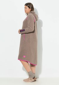 Robe marrone, soffice, lungo fino al ginocchio con cappuccio, dettagli rosa e logo. Presenta maniche lunghe, tasche laterali e una superficie strutturata.