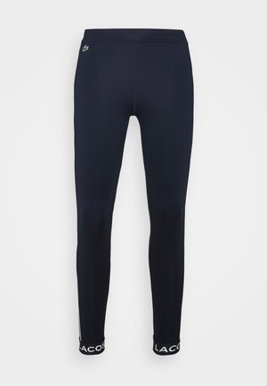 Leggings slim bleu marine avec logo Lacoste aux chevilles et petit emblème crocodile vert près de la taille.