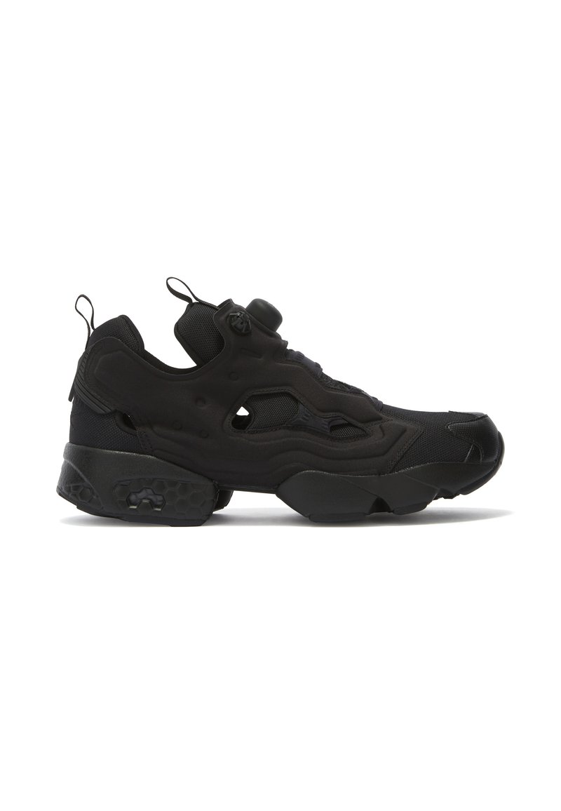 Sapatilhas pretas desportivas com um upper texturizado, detalhes hexagonais na sola, e um design slip-on com um fecho central para ajustamento.