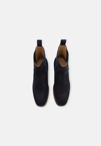 Paire de bottines Chelsea en suède noir avec panneaux latéraux élastiques et languettes de tirage, vues de dessus sur un fond blanc.