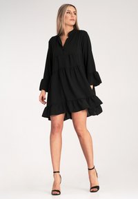 Czarna sukienka warstwowa z kołnierzykiem, długimi rękawami i falbankami. Lekki materiał, długość powyżej kolan, z luźnym krojem.