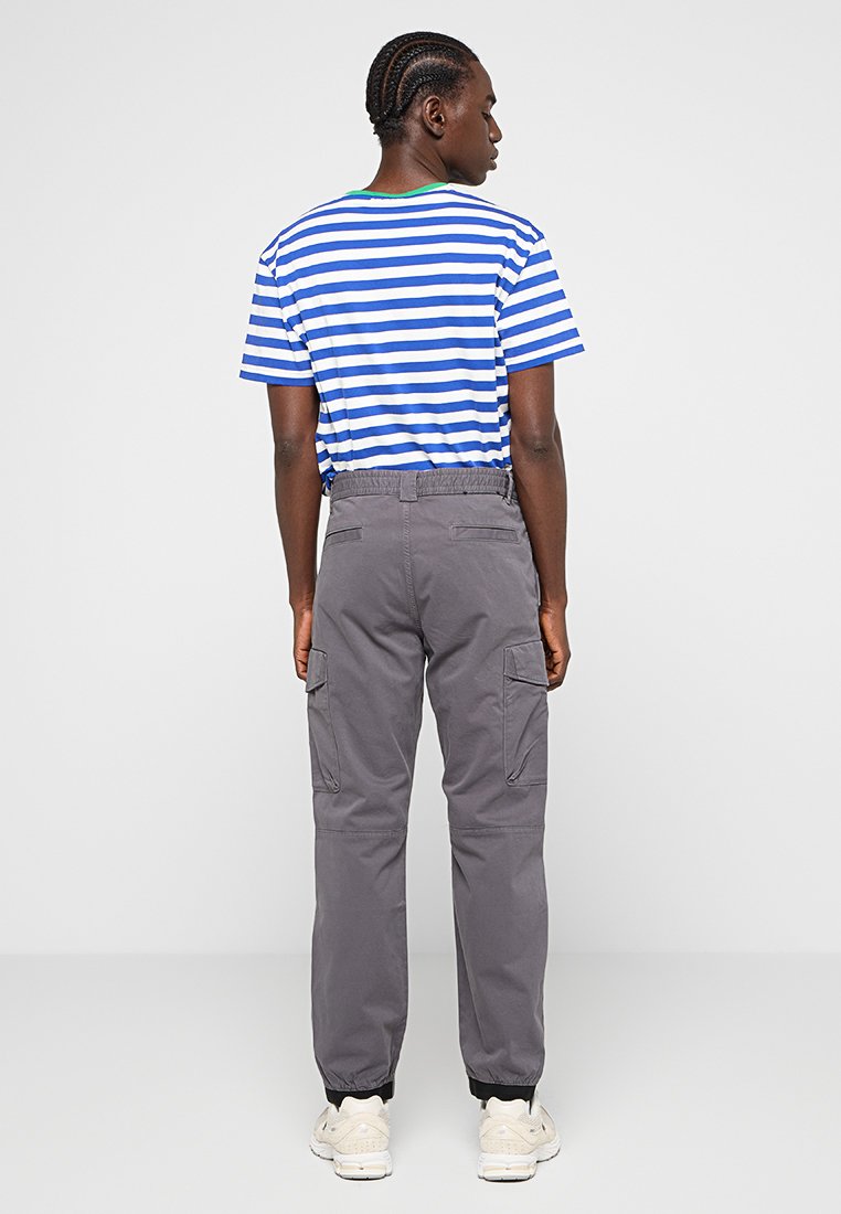 T-shirt rayé bleu et blanc avec un col vert, associé à un pantalon cargo gris avec des poches latérales et des poignets élastiques. Stylé avec des baskets.