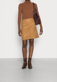 Brun ribbet højhalset sweater, lys suede A-linje nederdel, bordeaux håndtaske og brune ankelstøvler med spids tå og glat overflade.