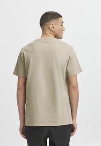 Light beige short-sleeve cotton t-shirt with a crew neck. The back shows a plain design with a relaxed fit and stitched hem.