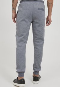 Szürke, textúrált joggers, szűkített szegéllyel a bokánál, gumis derékrésszel és egy hátsó zsebből áll. Fekete sportcipővel párosítva.