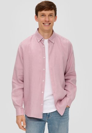 Helles rosa Langarmhemd mit Kragen, Fronttaschen und weißen Knöpfen, über einem weißen T-Shirt getragen und kombiniert mit hellblauen Jeans.
