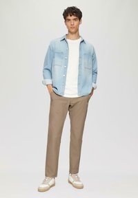 Jasnoniebieska koszula dżinsowa, biała koszulka z okrągłym dekoltem, beżowe spodnie i białe trampki z brązowymi akcentami. Gładkie tekstury, luźny krój.