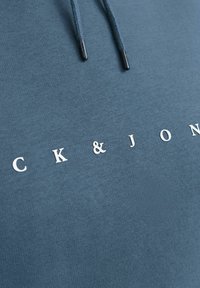 Blauwe katoenen hoodie met een koord in de capuchon, een gladde textuur en witte letters "CK & JON" op de borst.