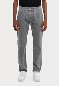 Jean en denim gris avec une coupe droite, design à cinq poches, détails de couture subtils et texture usée, associés à des baskets blanches.