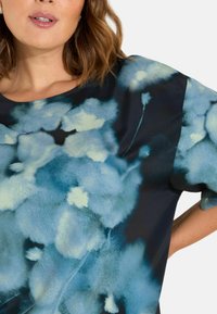 Kortärmad topp i mörkblått med ett blommönster i ljusblått och krämfärgad, med en mjuk textur och avslappnad passform.