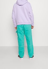 Violetti hupullinen pitkähihaisen collegepaita, yhdistettynä väljälahkeisiin turkooseihin cargo-housuihin, joissa on sivutaskut.