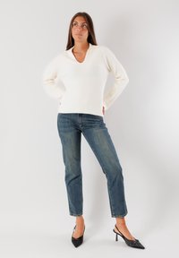 Maglione a coste color crema con scollo a V e maniche lunghe, abbinato a jeans in denim blu. Tacchi a punta nera completano l'outfit.