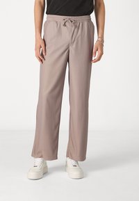 Pantalons gris côtelés avec une taille élastique et un cordon de serrage. Présentent une coupe décontractée et des poches latérales, assortis à des baskets blanches.