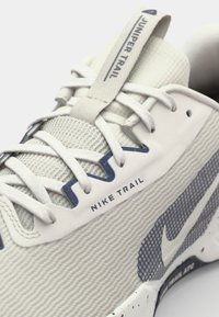 Nike Juniper Trail trkačka cipela, s teksturiranim sivim gornjim dijelom, plavim akcentima, bijelim vezicama i prošaranom potplatom sa detaljima brendiranja.
