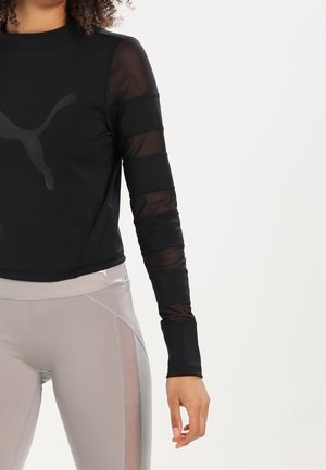 Schwarzes sportliches Langarmoberteil mit durchsichtigen Mesh-Ärmeln und einem dezenten Logo. Kombiniert mit grauen Leggings, die glänzende Seitenakzente aufweisen.