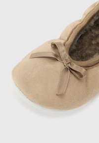 Beige mockasins i mocka med rund tå, med en liten rosettdetalj framtill och en ljust färgad texturerad sula.