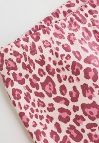 Närbild på tyg med rosa och mörkrosa leopardmönster och synlig söm på ljus bakgrund.
