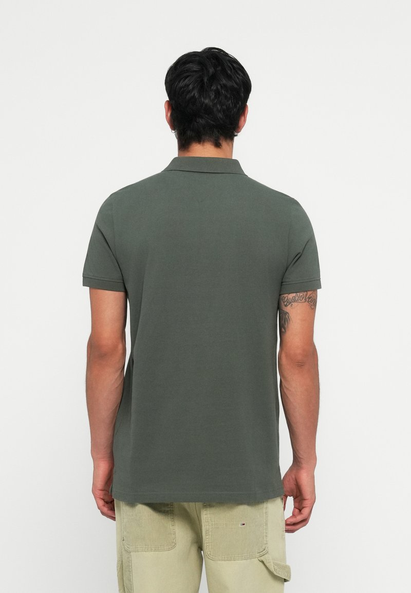 Donkergroen polo-shirt, korte mouwen, klassieke kraag, gladde katoenstructuur, gedragen met lichtbeige broek, gezien vanaf de achterkant.