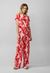 Jumpsuit rosso e pink a fantasia con maniche corte, vestibilità comoda, cintura elastica e pantaloni a gamba larga. Tessuto morbido con dettagli plissettati.