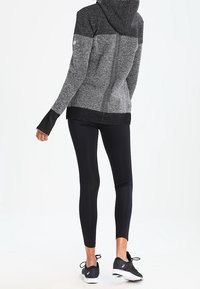 Grå og sort atletisk hættetrøje med hætte, lange ærmer og en struktureret finish, kombineret med sorte leggings og løbesko.