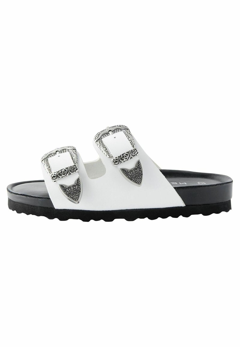 Vit halksandals med två justerbara remmar med intrikata silverfästen, en texturerad svart sula och ett slätt ovandelmaterial.