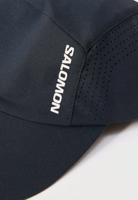 Μαύρο αθλητικό καπέλο Salomon με διάτρητες αεραγωγές και κυρτό γείσο, με το όνομα της μάρκας σε λευκά γράμματα στο μπροστινό πάνελ.