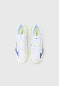 Zapatillas deportivas blancas con parte superior de malla texturizada, suela exterior amarilla y detalles en azul. Los cordones son blancos, con un logo en la lengüeta y la plantilla.