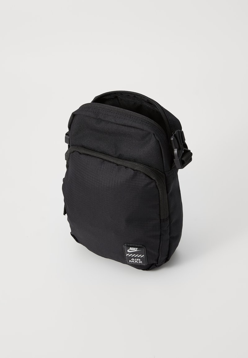 Schwarzer Nylon-Rucksack mit rechteckiger Form, Reißverschluss, verstellbarem Tragegurt und einem Markenaufnäher auf der Vorderseite. Strukturierte Oberfläche.