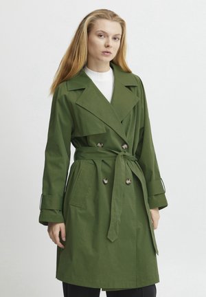 Groene trenchcoat met een dubbelgebreid ontwerp, grote kraag en strikceintuur. Het materiaal lijkt stevig; heeft zijzakken en details op de mouwen.