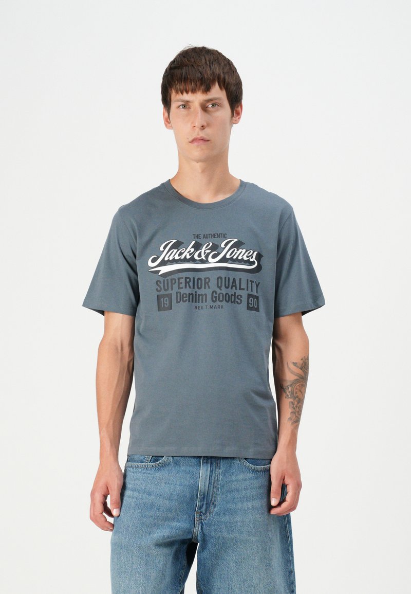 Grå bomulls t-skjorte med korte ermer, med et grafisk trykk i hvit og svart tekst som sier "Jack & Jones Superior Quality Denim Goods."