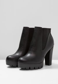Stivaletti neri alla caviglia in pelle liscia con pannelli laterali elastici, un tacco spesso e una suola platform con motivo a battistrada testurizzato.