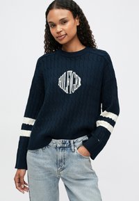 Pulover din lână, tricotat în stil navy, cu guler rotund și un logo brodat alb. Dispune de accente în dungi albe și navy pe mâneci.